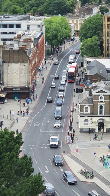 A street scene in Balham with a view of a clock tower on a historic church building surrounded by trees and residential houses, under a bright blue sky with some white clouds. In the foreground, sever